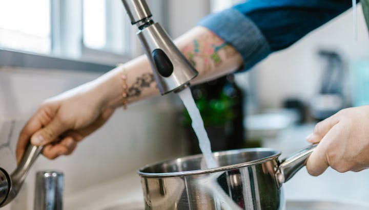 Water fills a pot from a kitchen faucet, while a person holds it in a sink.