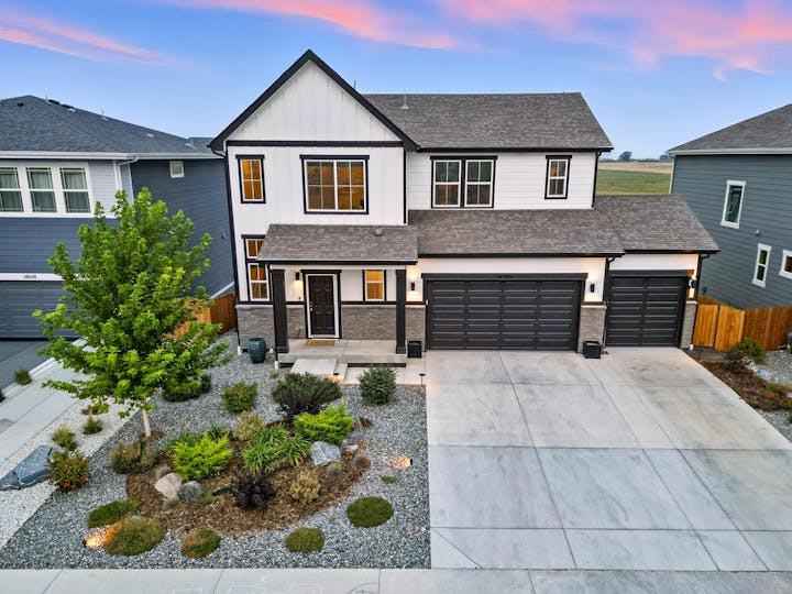 A modern two-story house with a landscaped yard, stone accents, and multiple garage doors, set against a scenic backdrop.