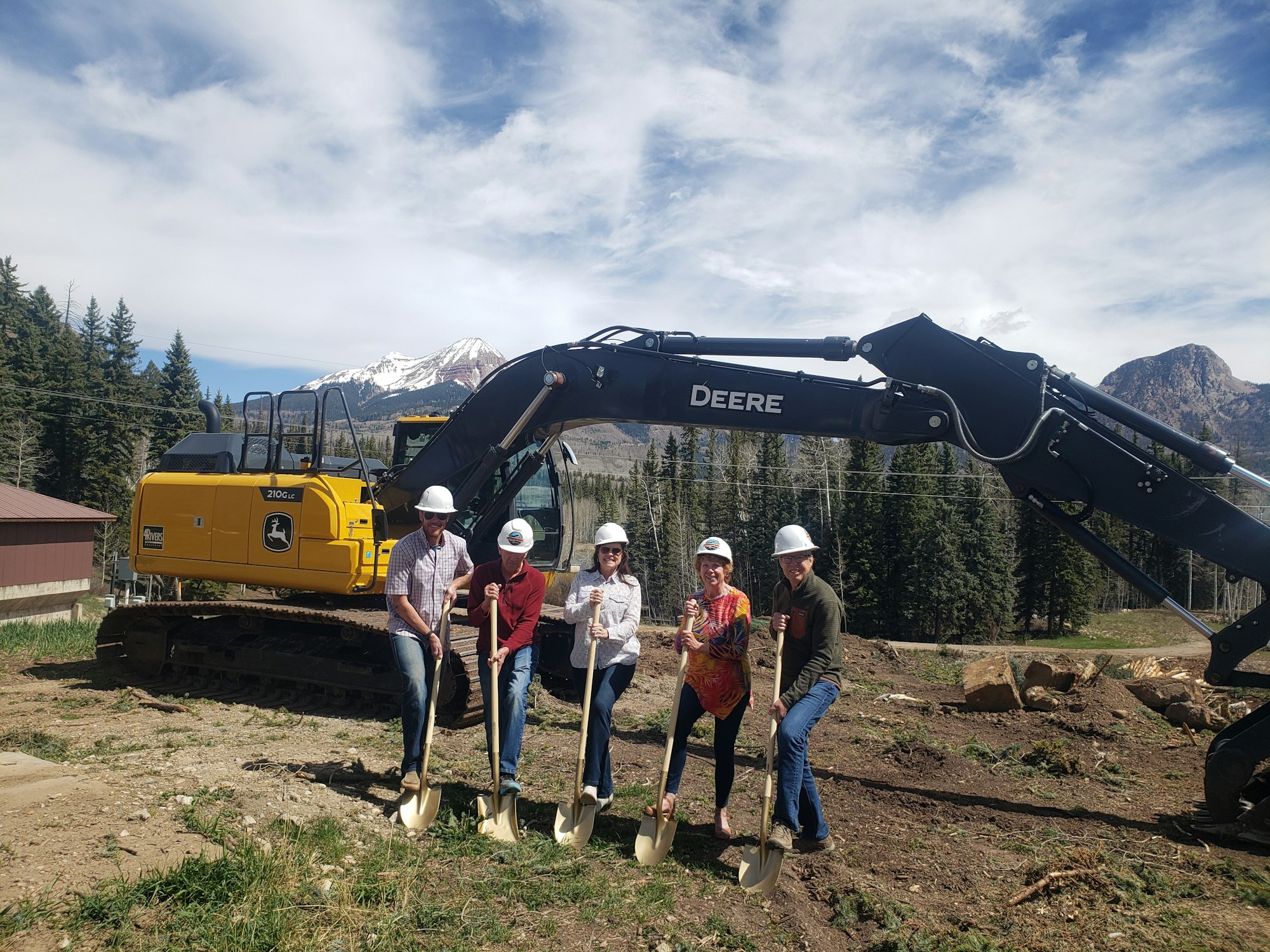 Eric Hassel, along with Board members Mark Gebhardt, Susan Voorhees, Sharon Henschen, and John Ogier with gold shovels, excavating equipment, and the mountains in the background