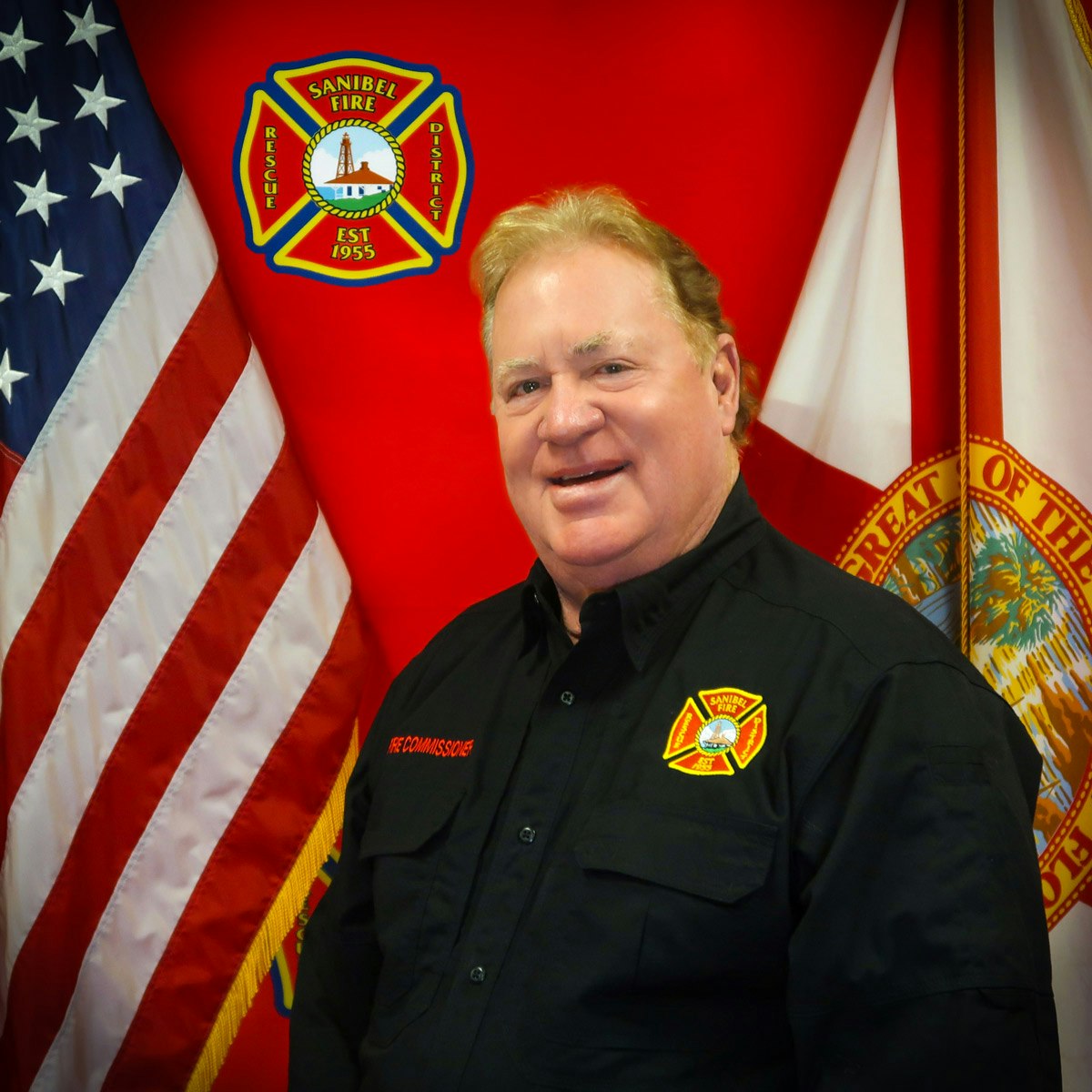 A person in front of American and state flags, wearing a Sanibel Fire District shirt with badges.