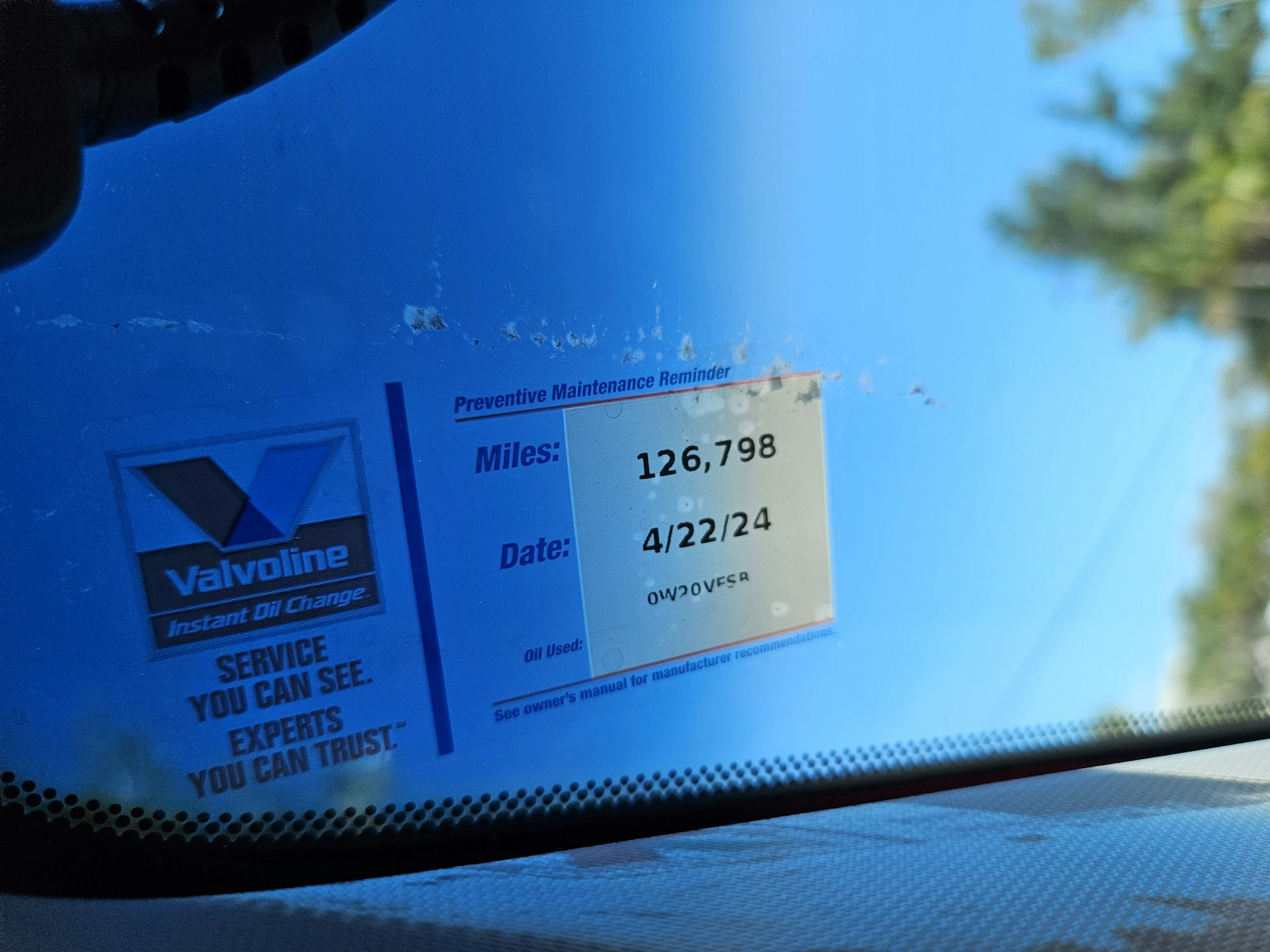 Oil change sticker on a windshield showing service due at 126,798 miles or by 4/22/24.
