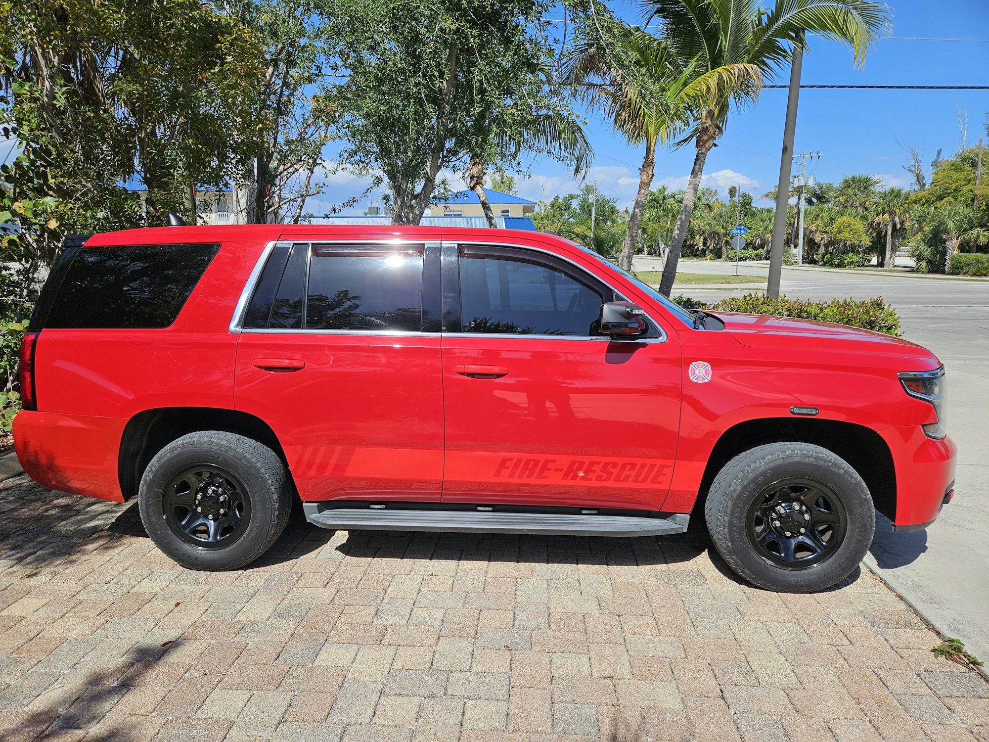 A red fire-rescue SUV parked on a sunny street with palm trees in the background.