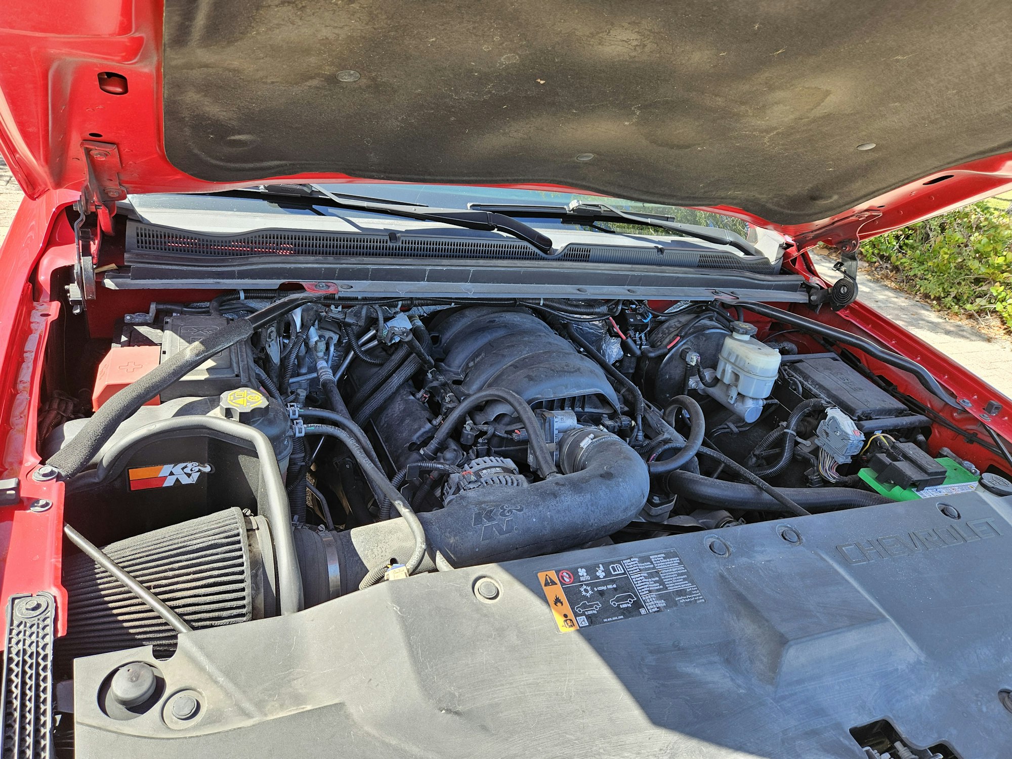 A red car's open hood revealing its engine bay with various components.