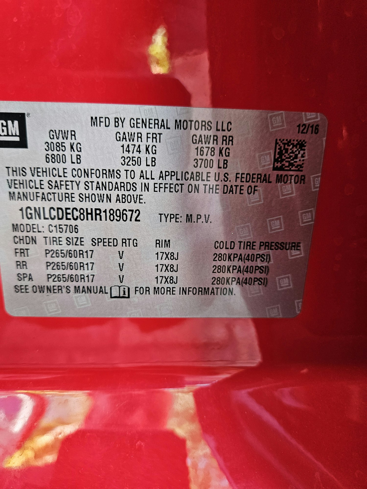 A vehicle information sticker with data such as tire size, pressure, and VIN, on a red background.