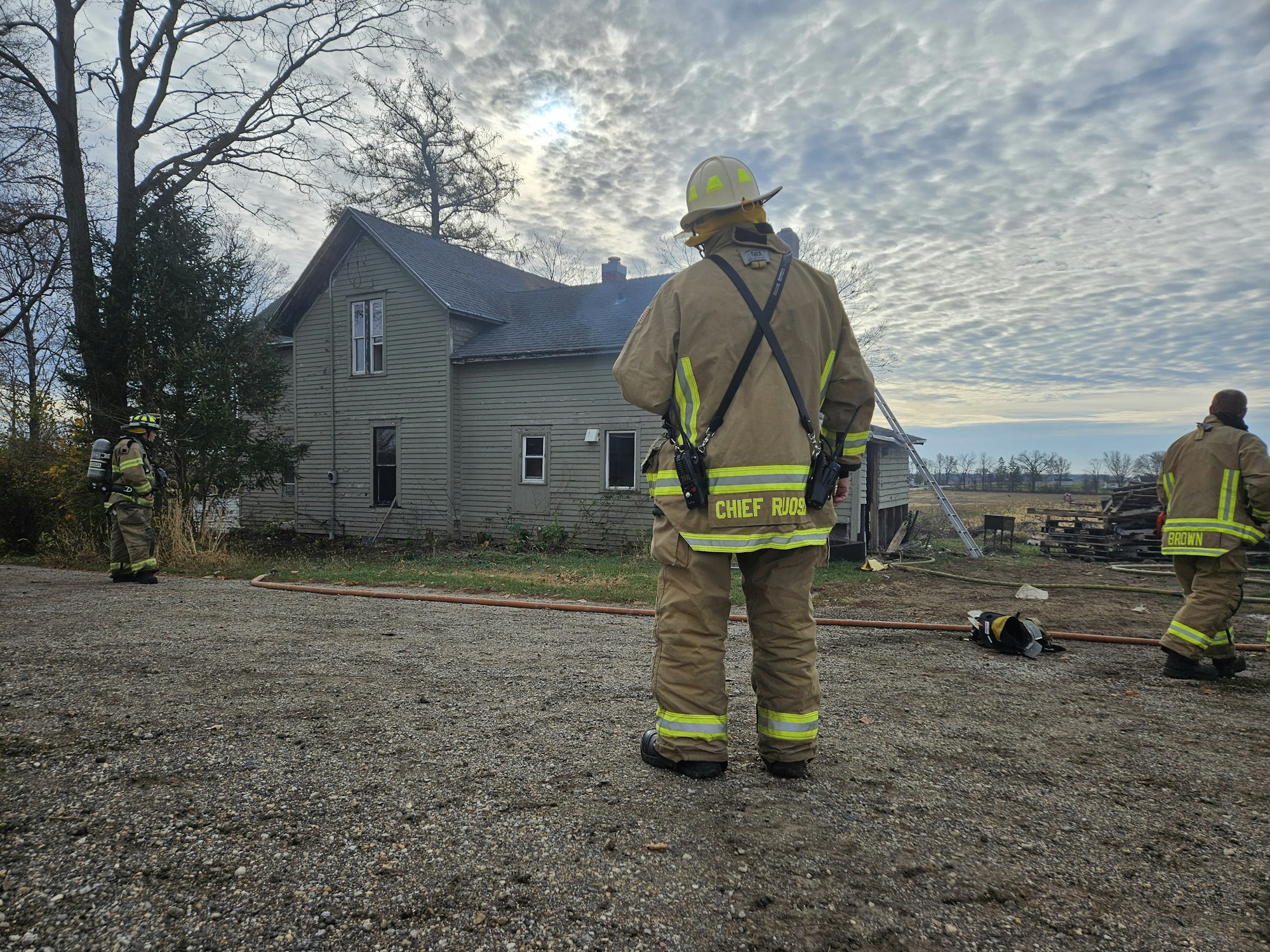 Firefighters in gear outside a house with a cloudy sky overhead.