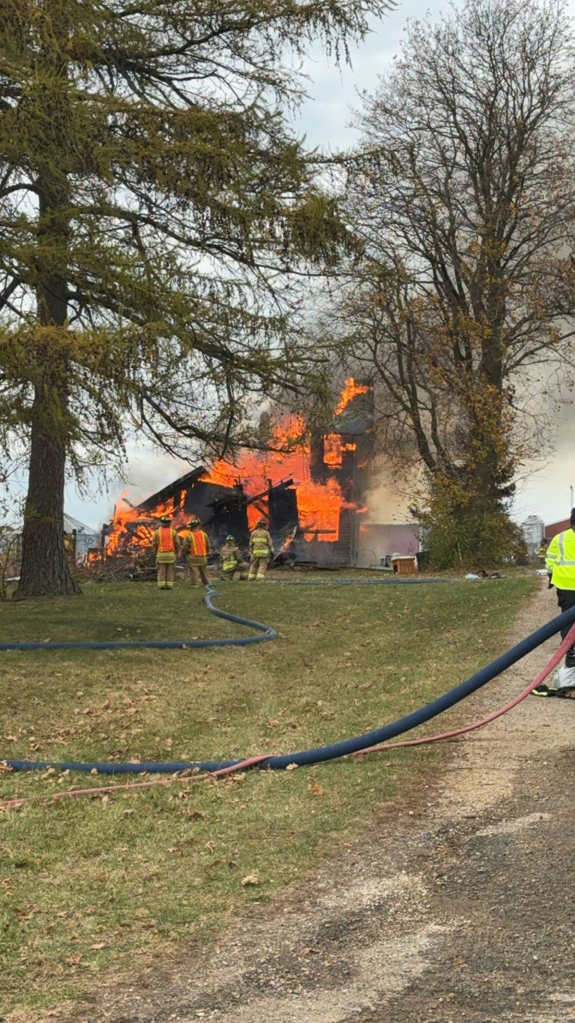 A house engulfed in flames with firefighters working to extinguish the fire.