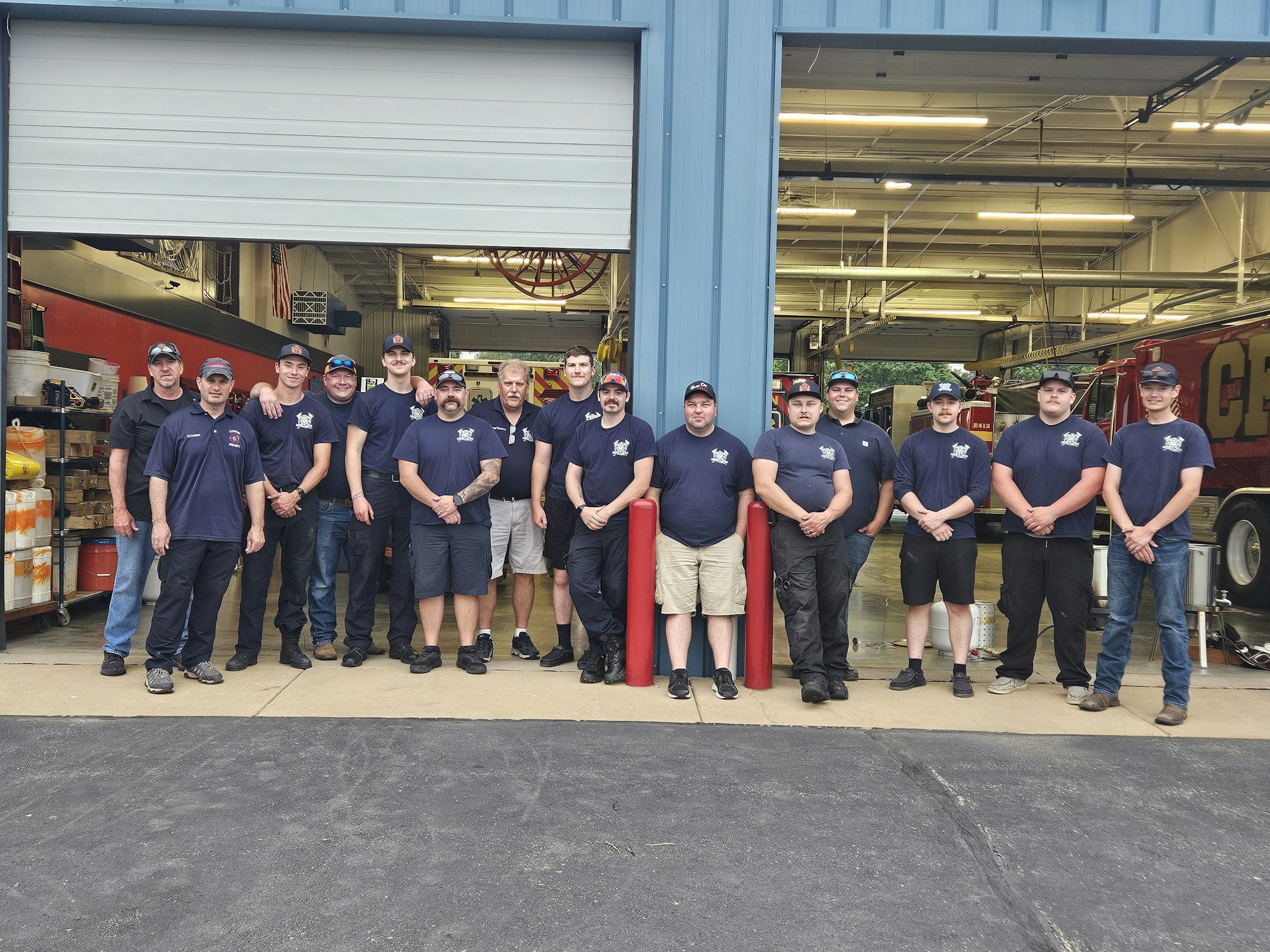 A group of firefighters posing for a photo outside a fire station.