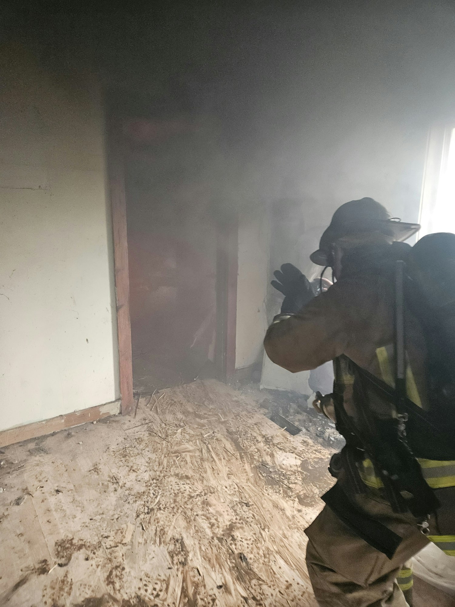 A firefighter in smoke-filled room, assessing a fire-damaged interior.