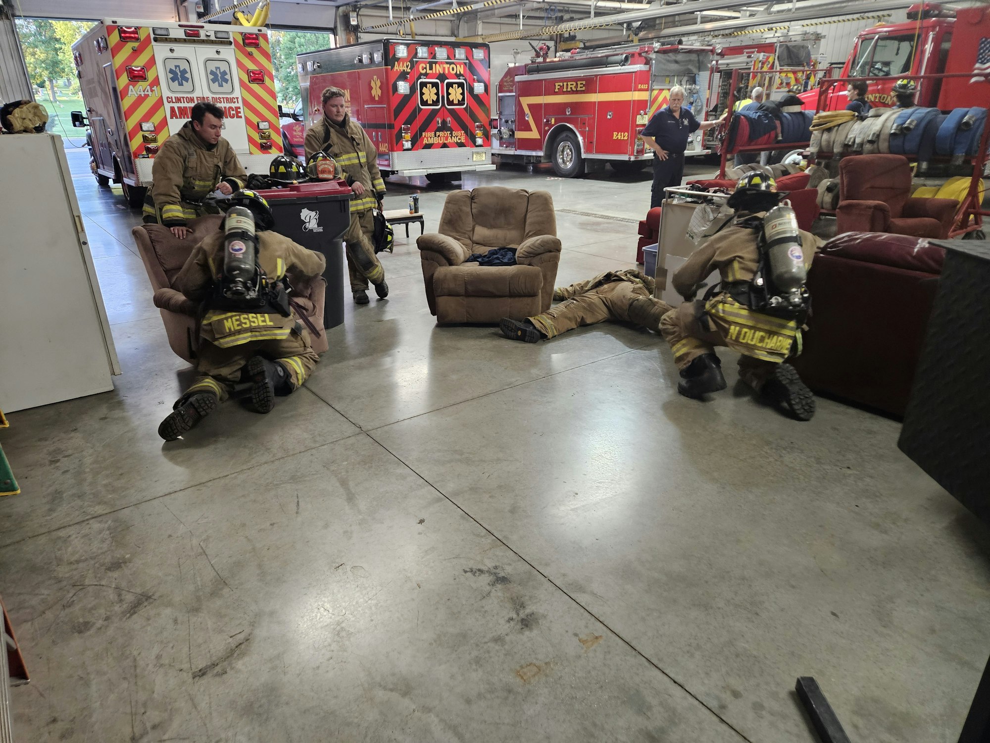 Firefighters in gear in a fire station, engaged in a training or briefing session.