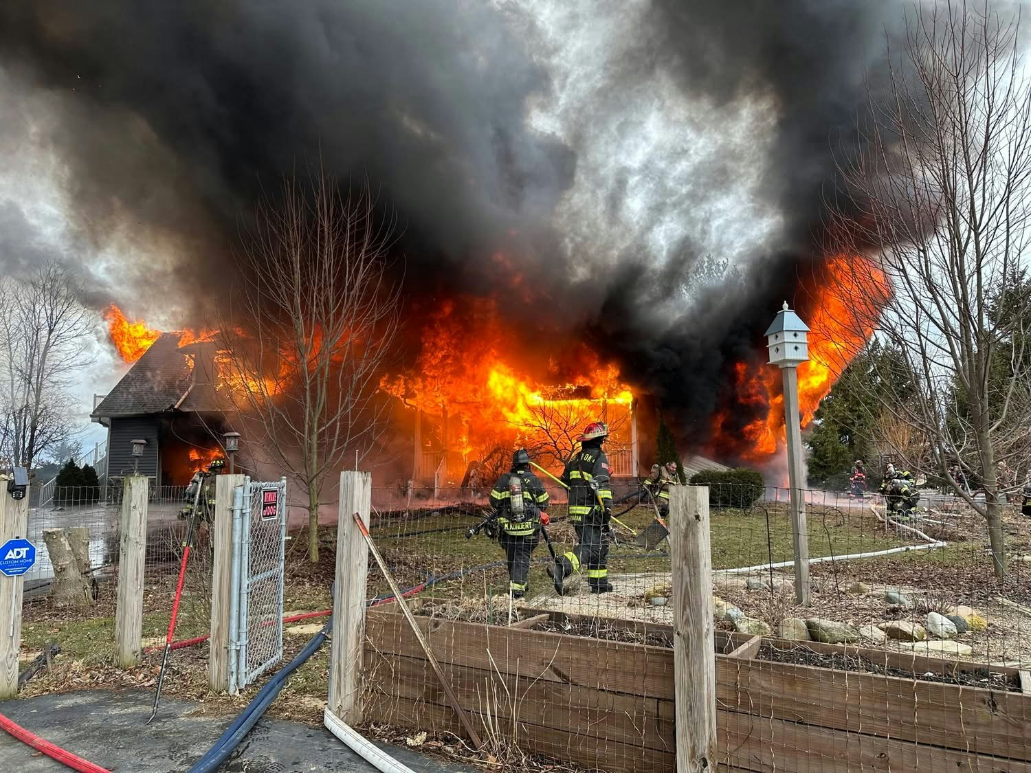 A house is engulfed in flames and thick smoke, with firefighters actively battling the fire in a residential area.