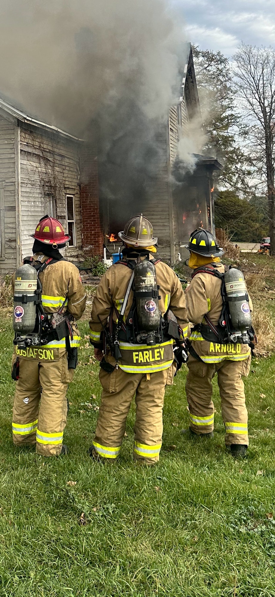 Firefighters standing before a burning house, preparing to extinguish the fire.