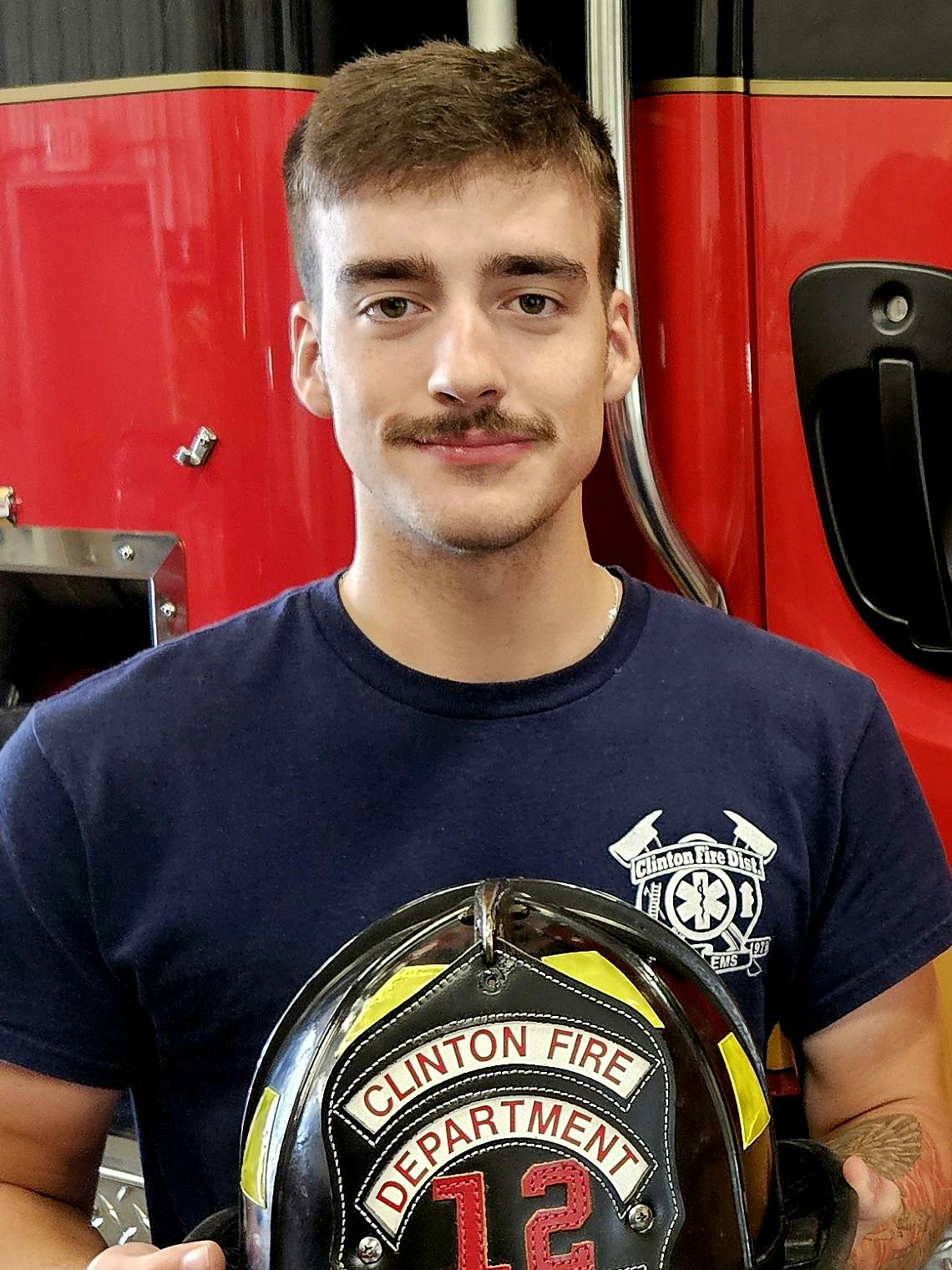 Firefighter holding a helmet next to a Clinton Fire District fire truck.