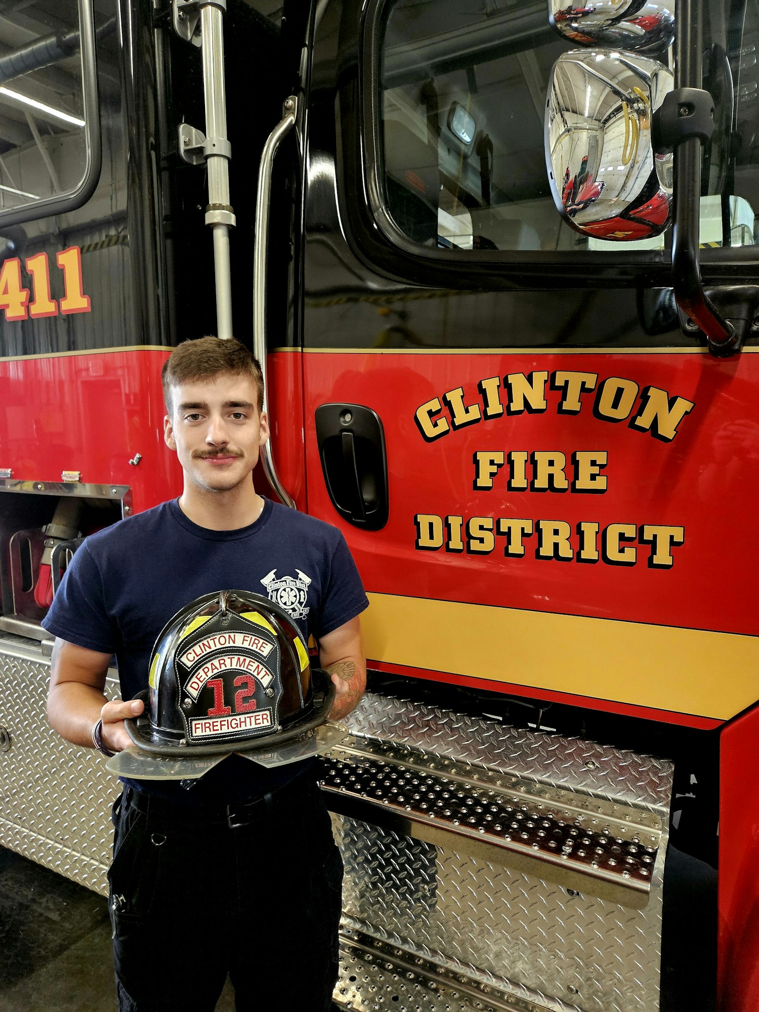 Firefighter holding a helmet next to a Clinton Fire District fire truck.