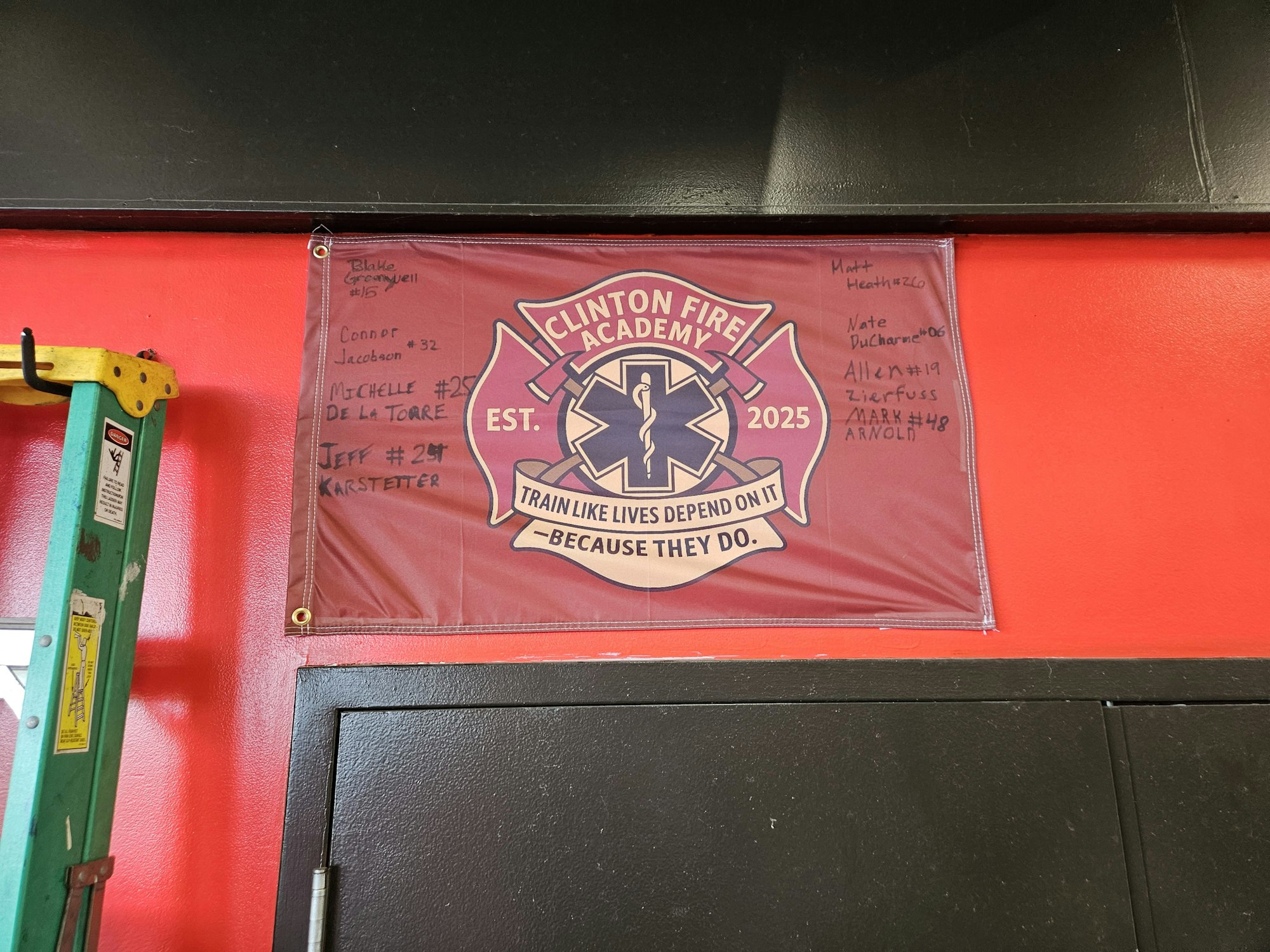 A "Clinton Fire Academy" banner with signatures and a ladder on a red wall.