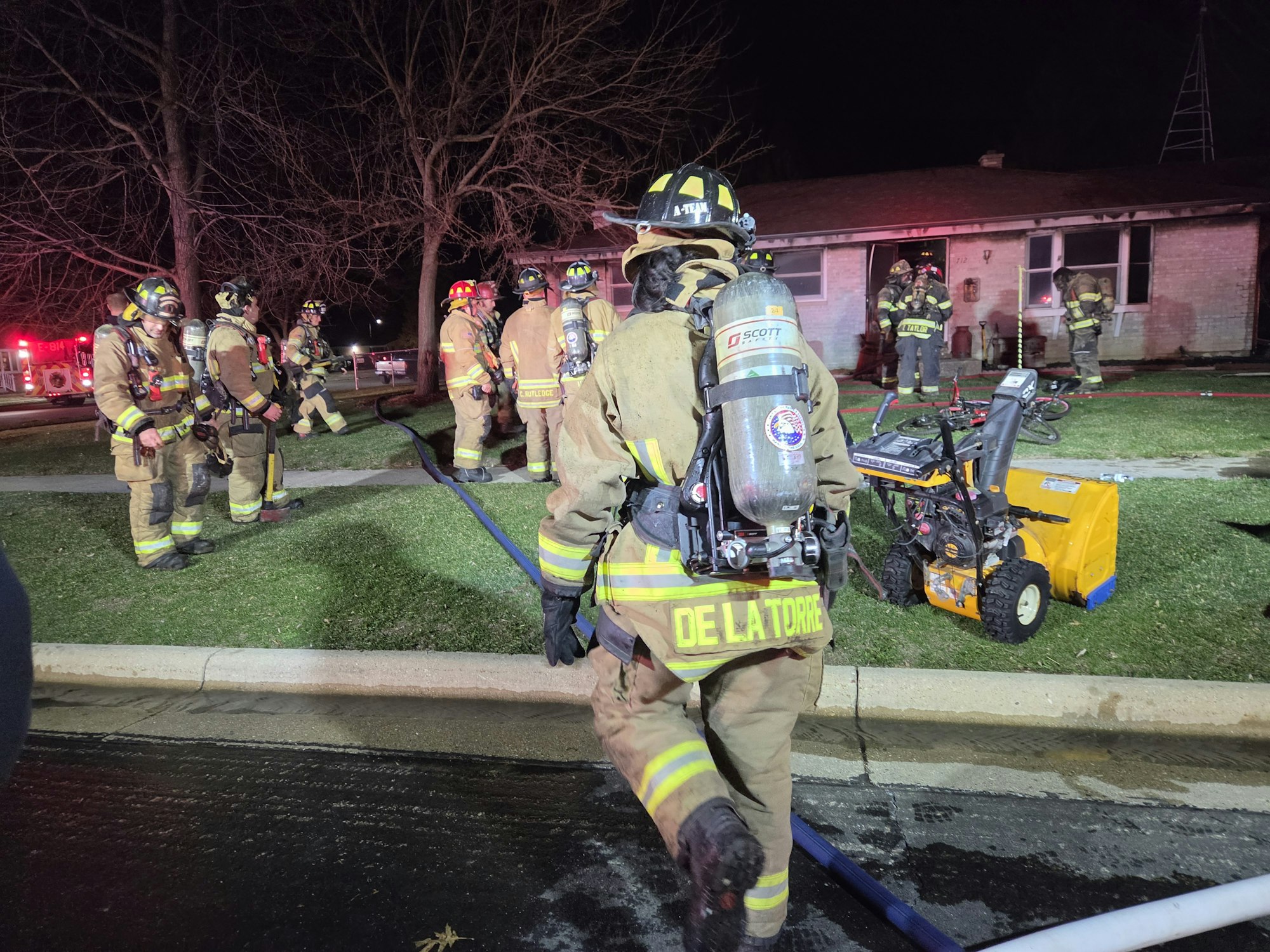 Firefighters respond to an incident at night, with equipment and fire hoses visible, actively working on the scene.