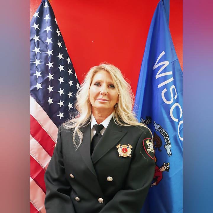 A person in uniform with badges in front of US and Wisconsin flags.