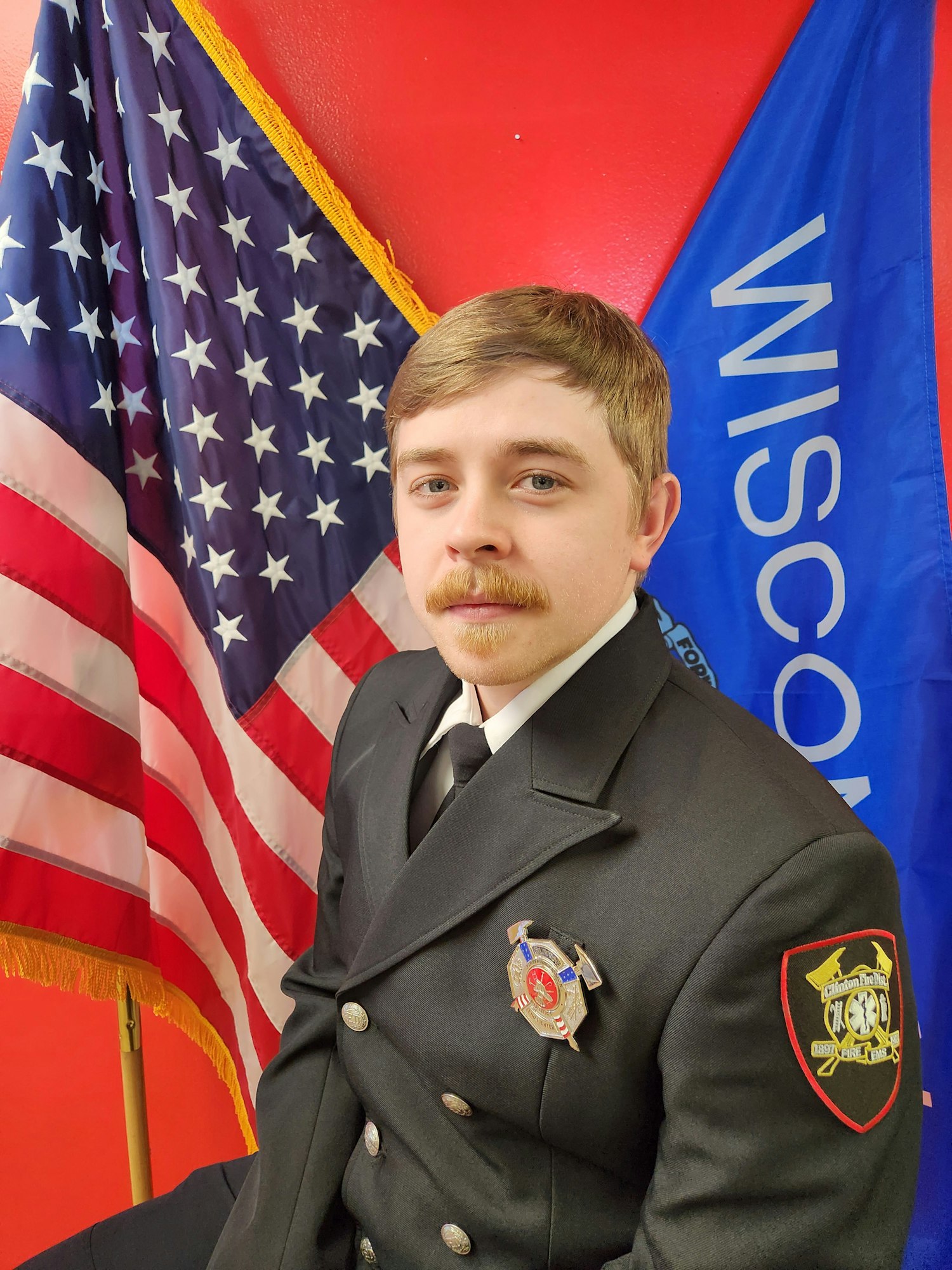 A person in uniform in front of Wisconsin and American flags.