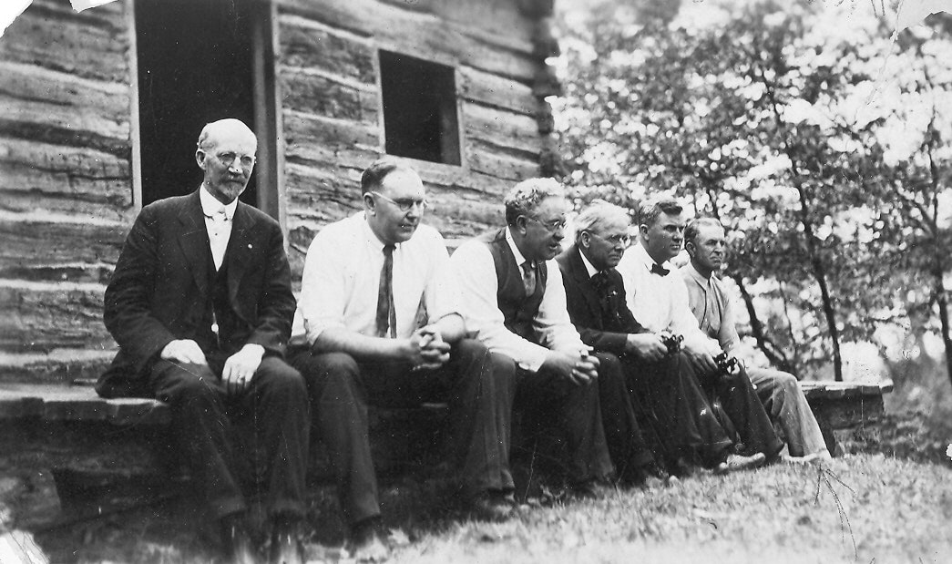 May contain: people, person, adult, male, man, architecture, building, housing, accessories, formal wear, tie, cabin, house, log cabin, outdoors, shelter, and glasses