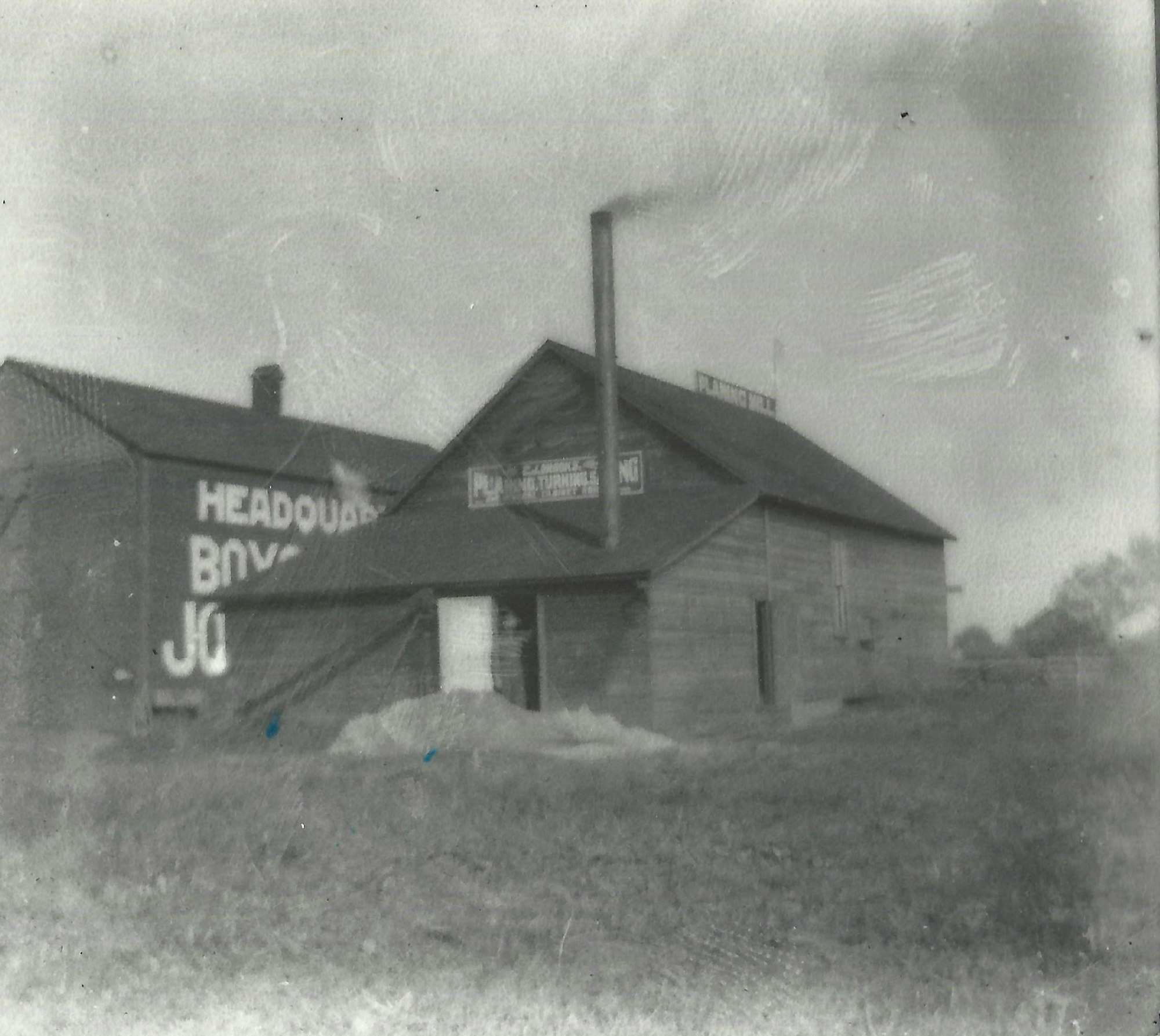 A vintage black-and-white photo of a wooden building, with signs indicating it as the "Headquarters" for a business.