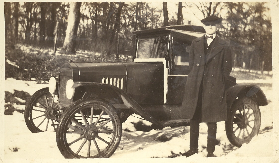 May contain: antique car, car, model t, transportation, vehicle, machine, spoke, clothing, coat, wheel, adult, male, man, and person