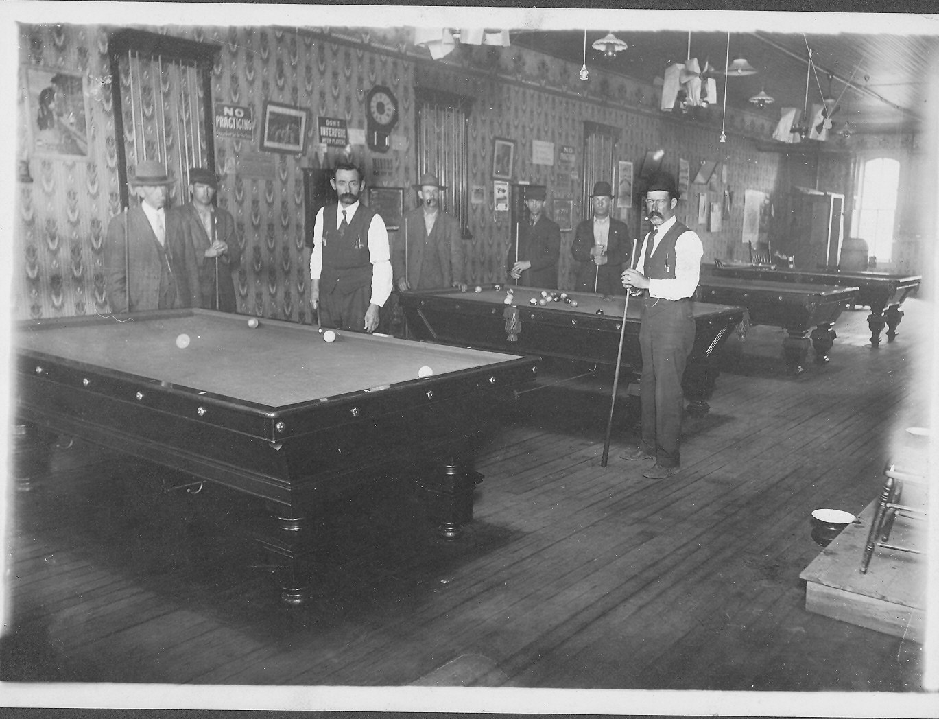 May contain: furniture, table, indoors, person, desk, clothing, hat, footwear, shoe, billiard room, pool table, room, lamp, art, and painting
