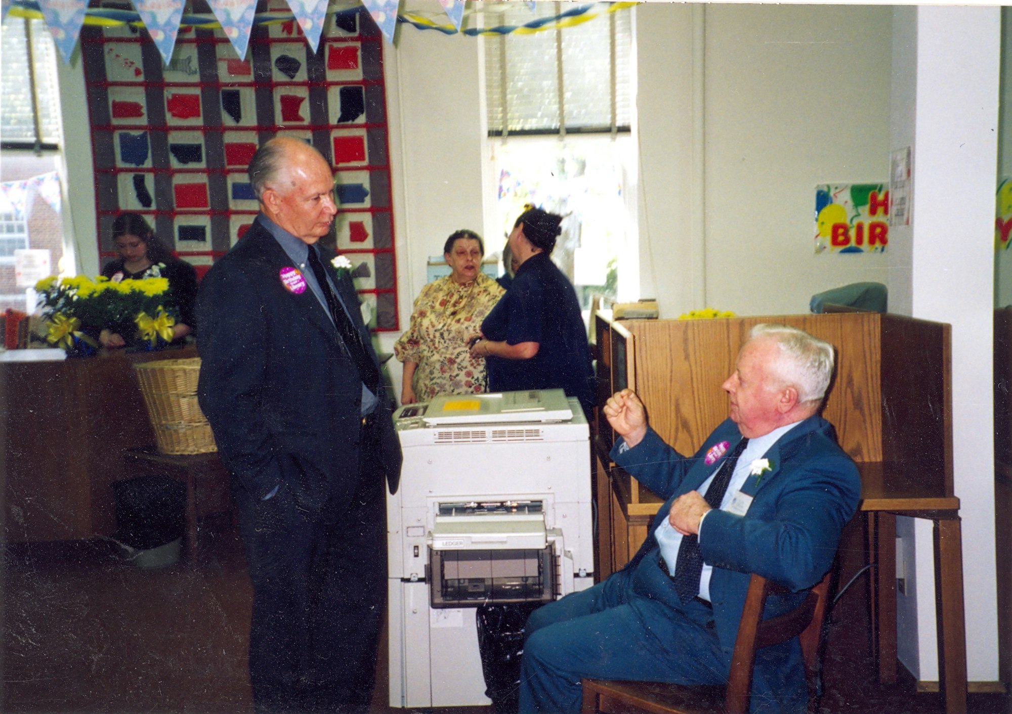 May contain: clothing, formal wear, suit, flower, flower arrangement, plant, flower bouquet, potted plant, computer hardware, electronics, hardware, adult, male, man, person, female, woman, plywood, wood, and coat