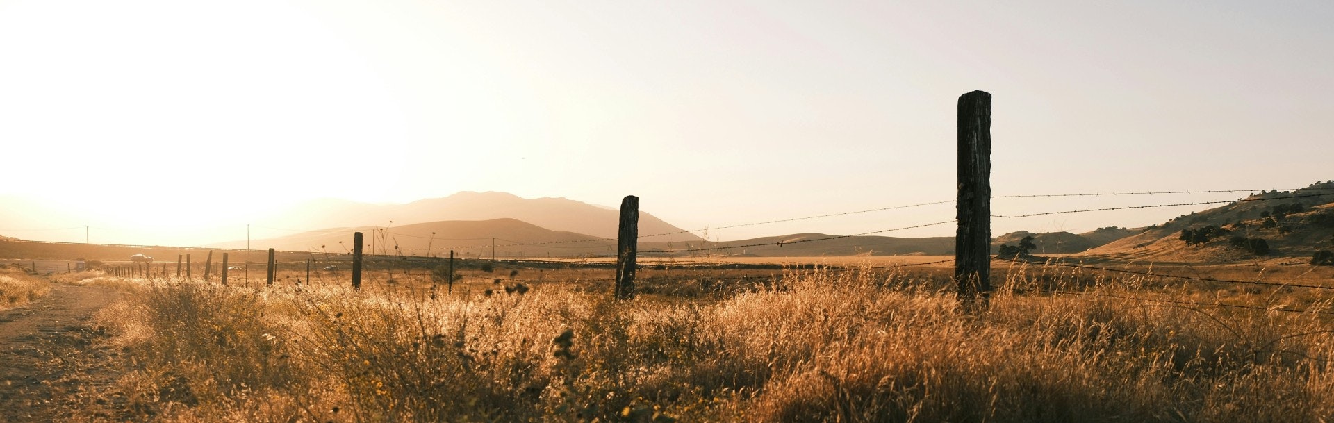 A serene countryside at sunset with hills, dry grass, and a barbed wire fence.