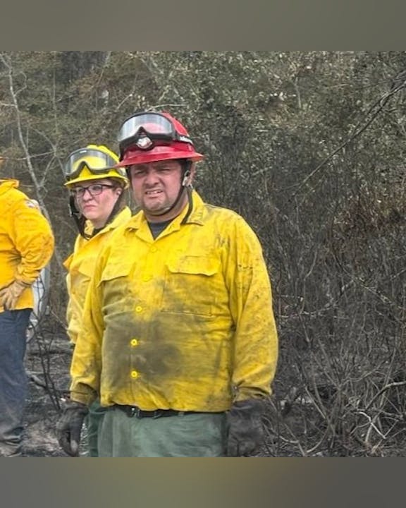 Firefighters in yellow gear and helmets standing in a burnt forest area.