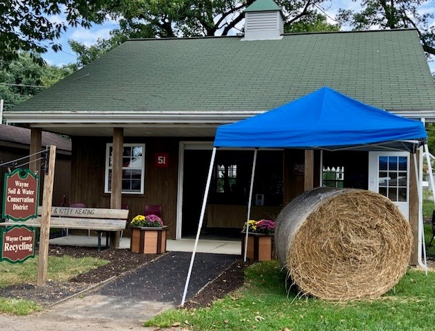 Small building with green roof, blue canopy, hay bale, and signage for Wayne Soil & Water Conservation District, Wayne County Recycling.