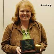 A person holding an award plaque and a gold apple, with the name "Linda Lang" written beside them.