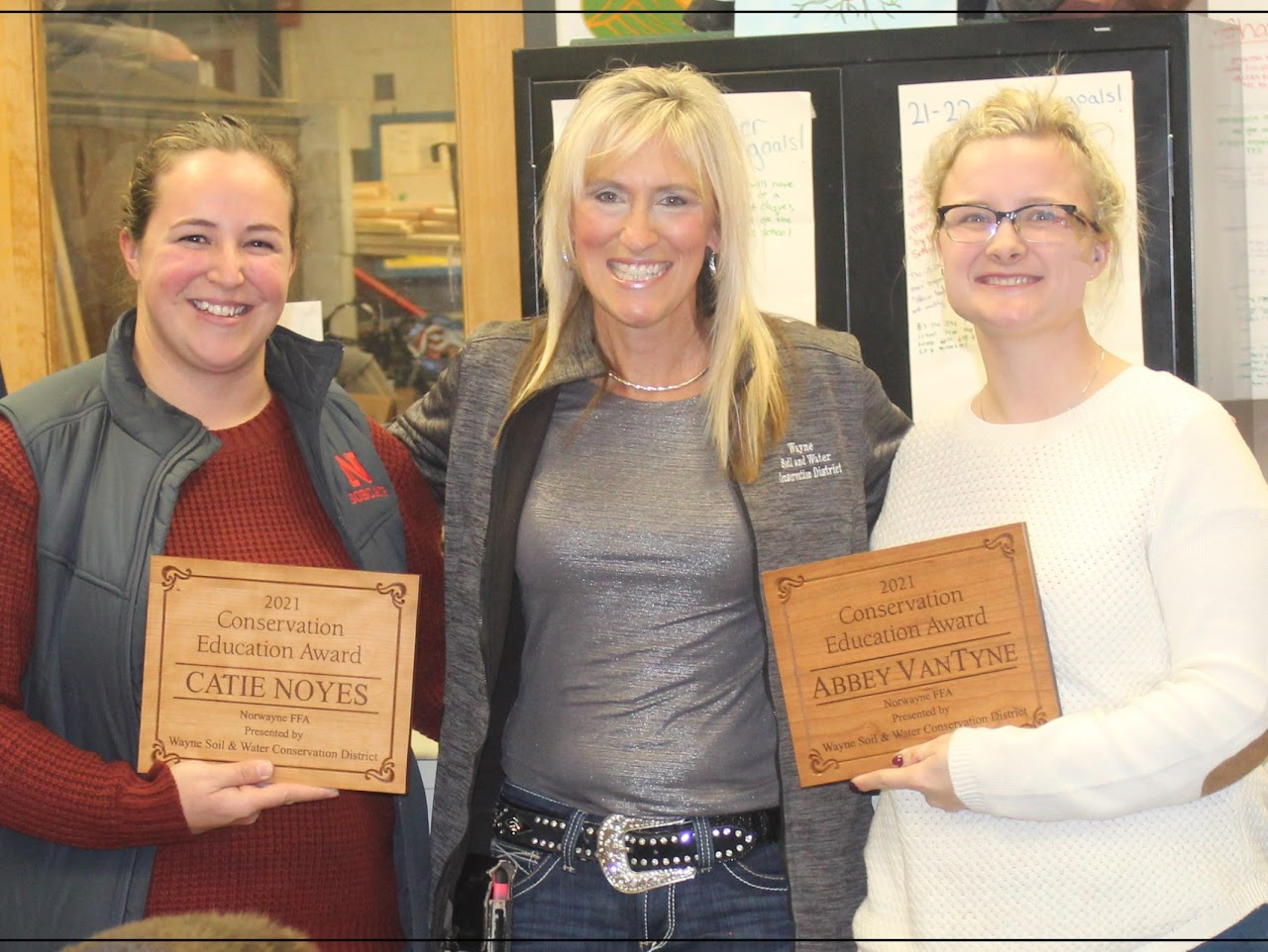 Three people smiling, holding Conservation Education Awards for 2021.