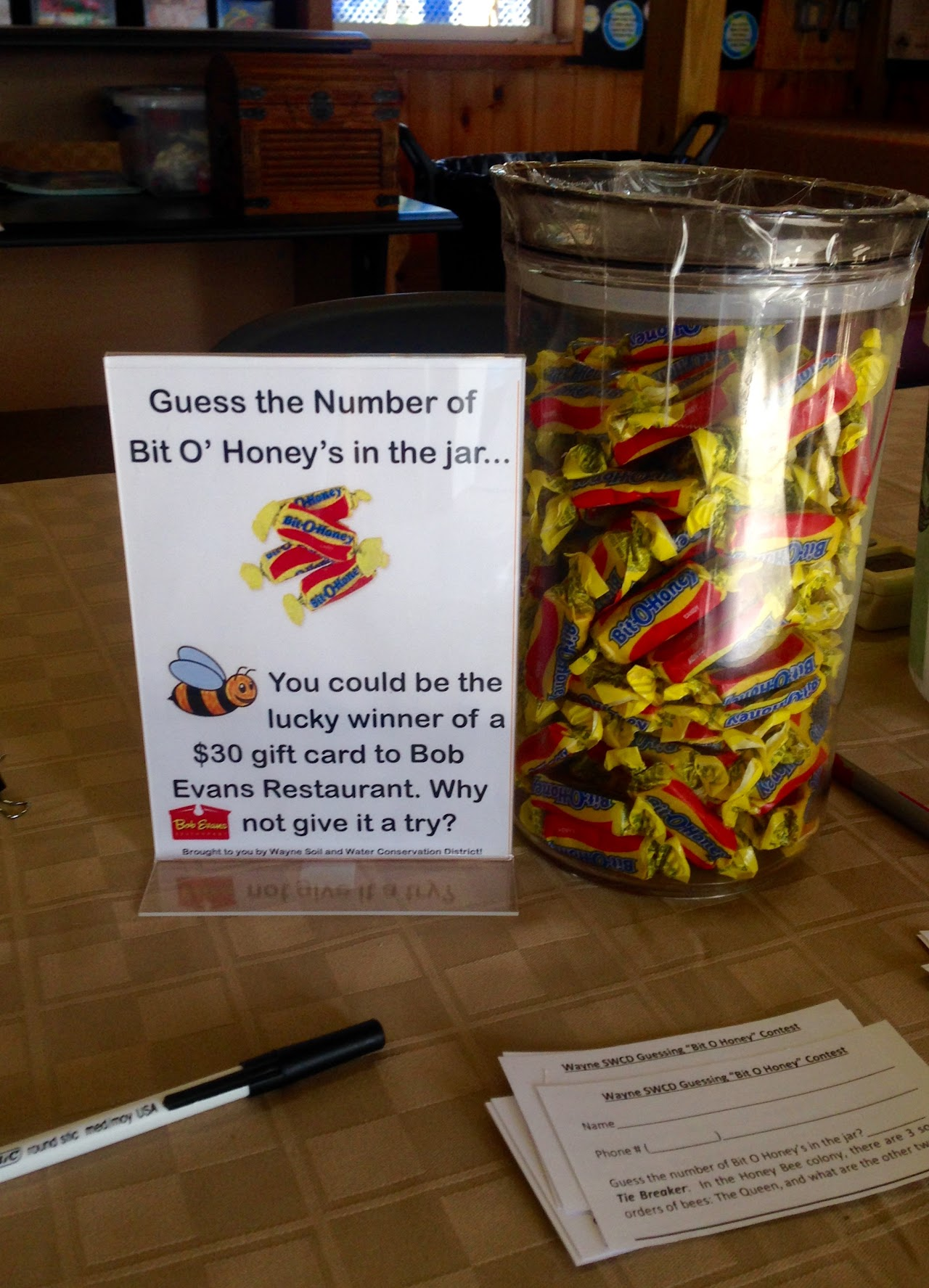 A "Guess the Number of Bit O' Honey" contest with a large candy jar and a sign offering a $30 Bob Evans gift card prize.
