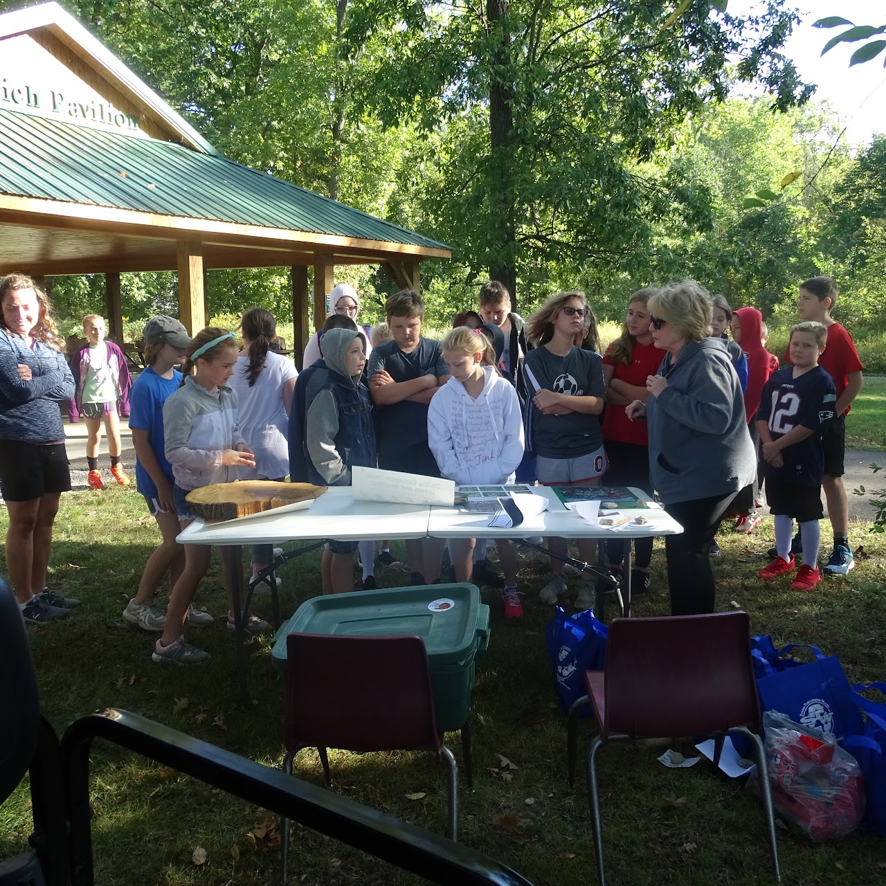 A group of people gathered around a table outdoors, near a pavilion.