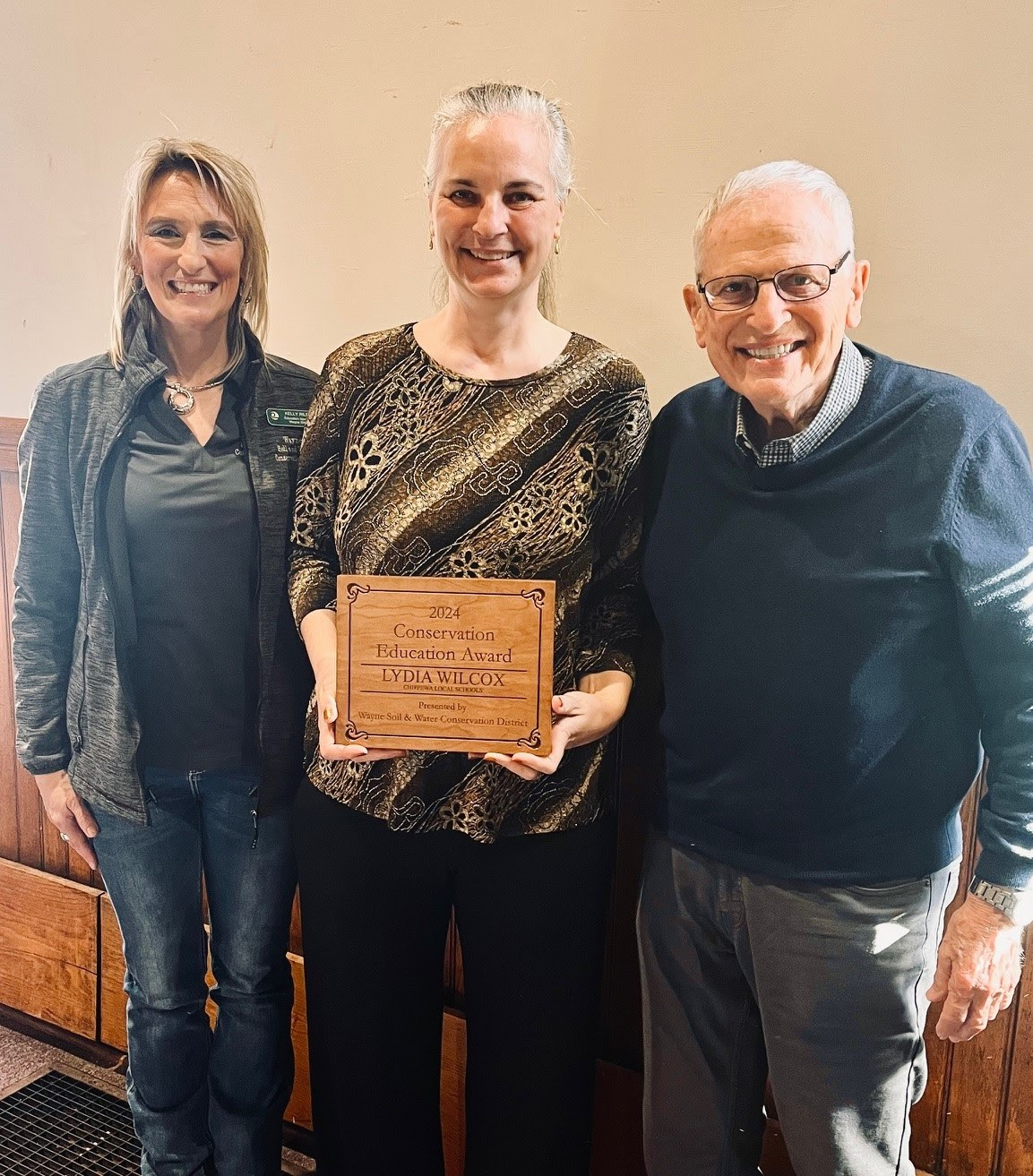 Three people smiling, the center person holding a "2024 Conservation Education Award."