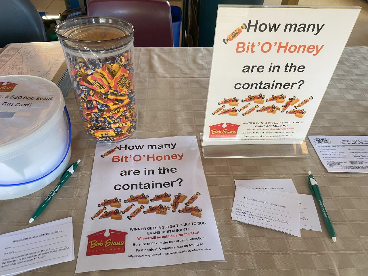 A guessing contest table with a jar of Bit-O'Honey candies, entry forms, pens, and a sign for a chance to win a Bob Evans gift card.