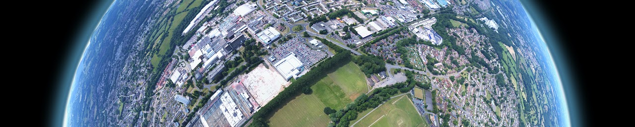 Aerial view of a landscape with urban and rural areas, featuring buildings, roads, and green fields, with a curved Earth effect.