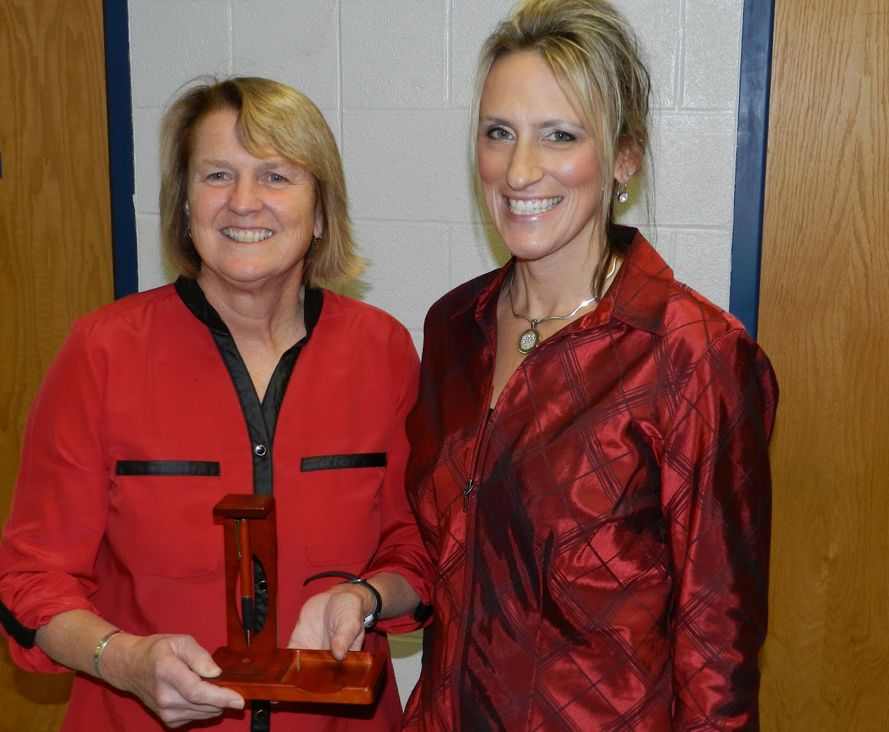 Two people smiling, with one holding a small award or trophy.