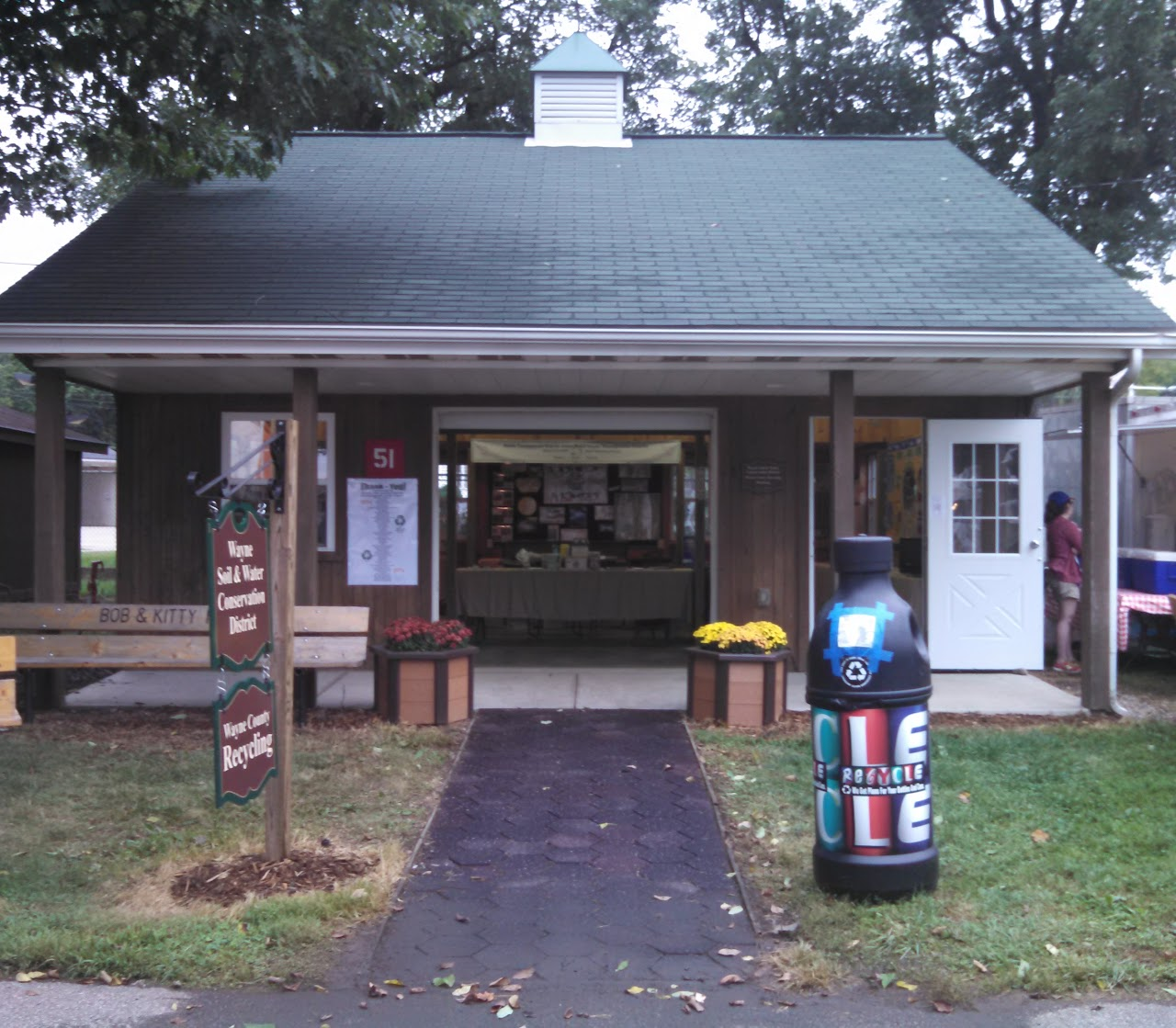 Small building with "Wayne Soil & Water Conservation District" sign, benches, a recycling bin, and displays inside.