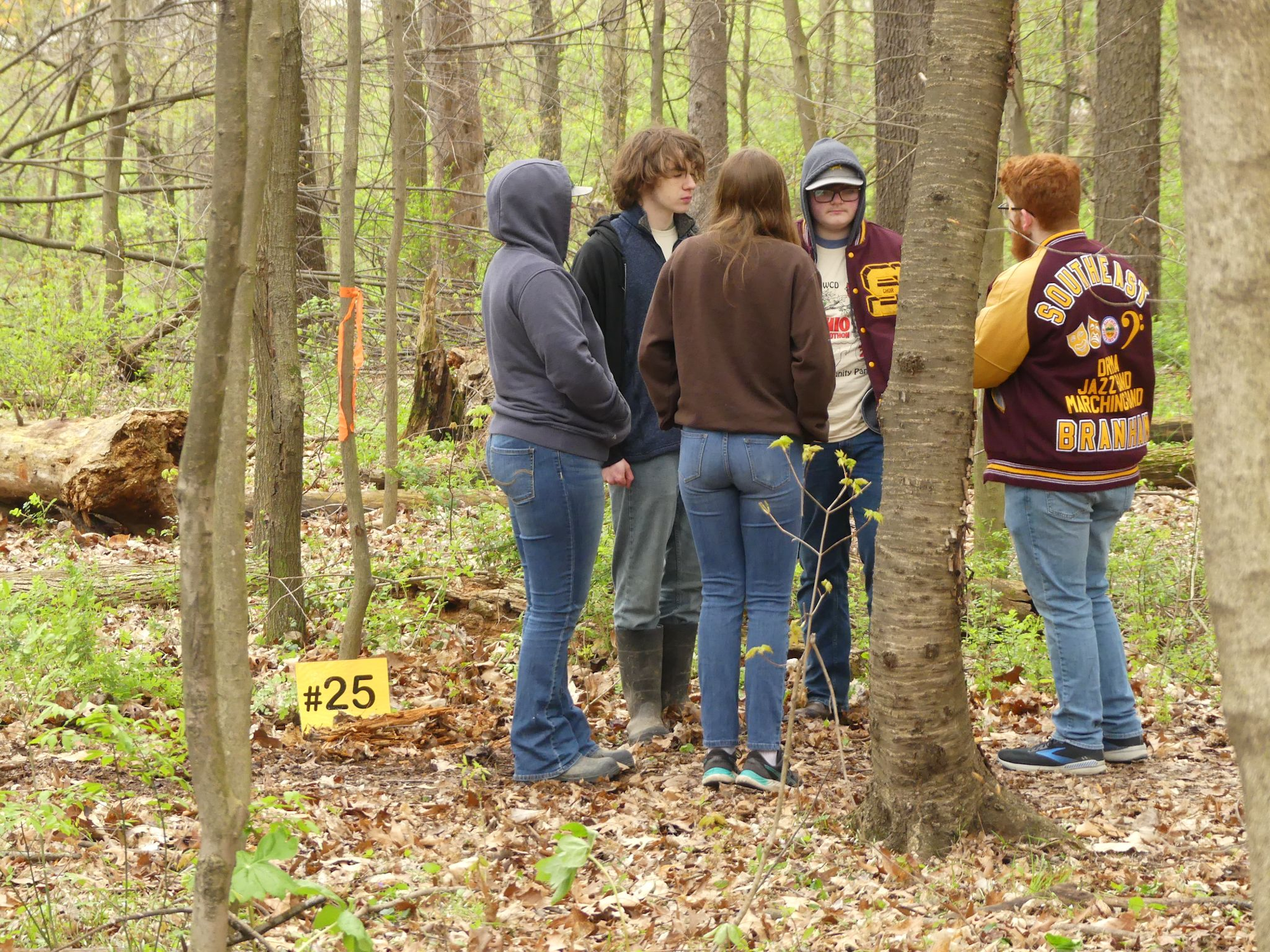 A group of people standing together in a wooded area near a sign labeled "#25".
