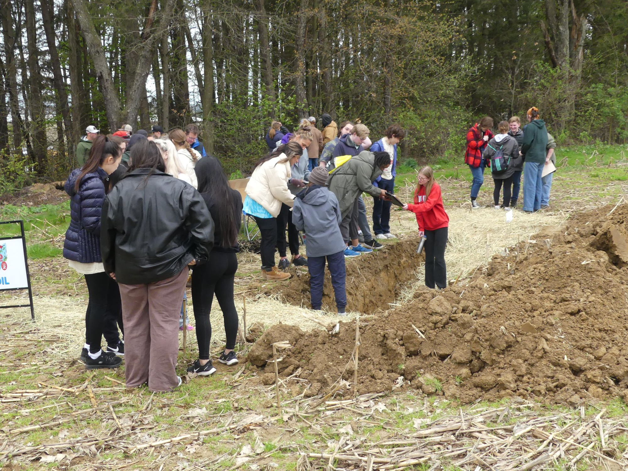 A group of people gathered around a trench outdoors, possibly participating in an activity or event.