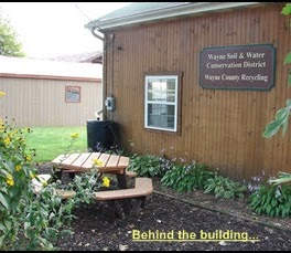 A wooden building with a sign for Wayne Soil & Water Conservation District and a picnic table surrounded by plants.