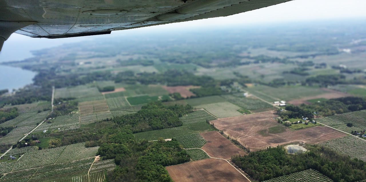 Aerial view of patchwork farmland and fields with a lake in the distance, visible under a plane's wing.