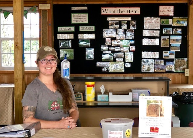 A person sits at a table in front of a bulletin board displaying hay information.