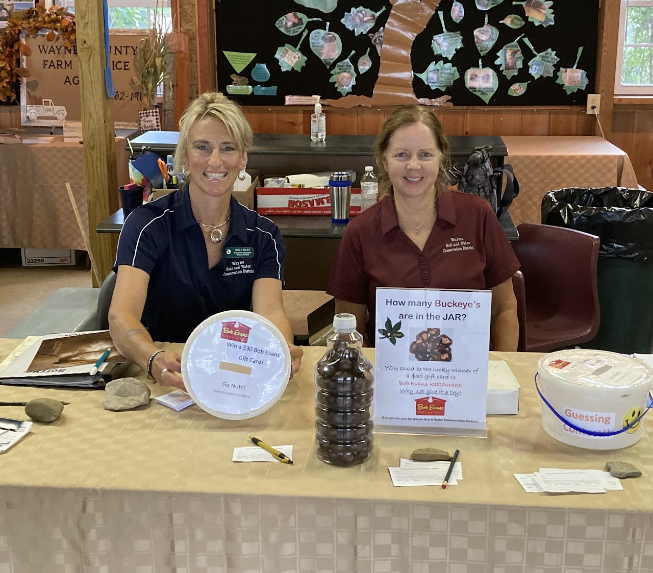 Two people at a table with a guessing game about buckeyes in a jar, offering a Bob Evans gift card as a prize.