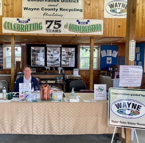 A person sits at a conservation and recycling info booth for Wayne County, celebrating 75 years of conservation.