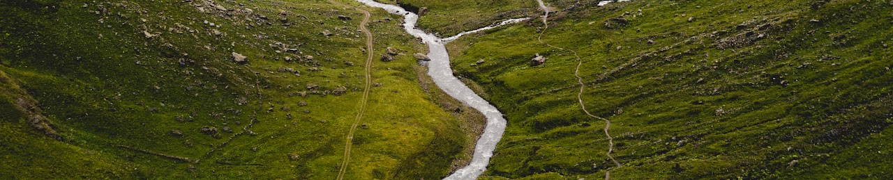 A narrow river winding through a green valley with rocky slopes.