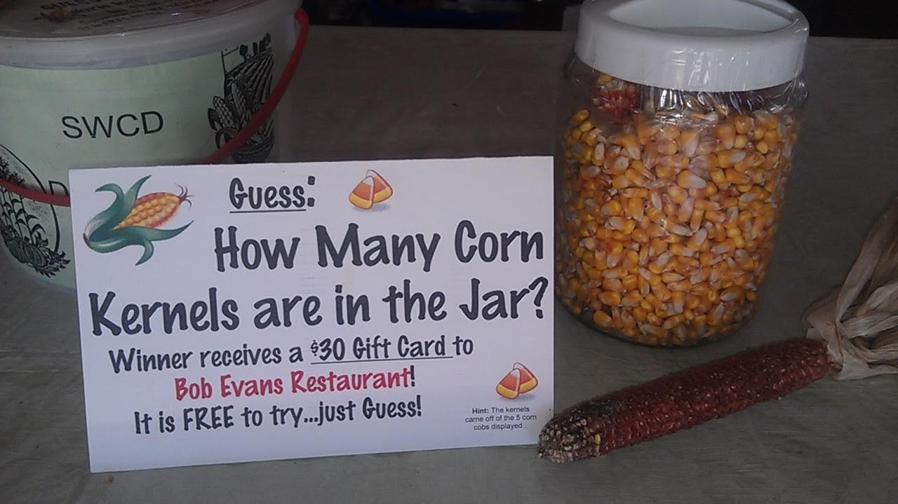 A sign invites guesses on corn kernels in a jar to win a $30 Bob Evans gift card. A husked corn cob lies beside the jar.