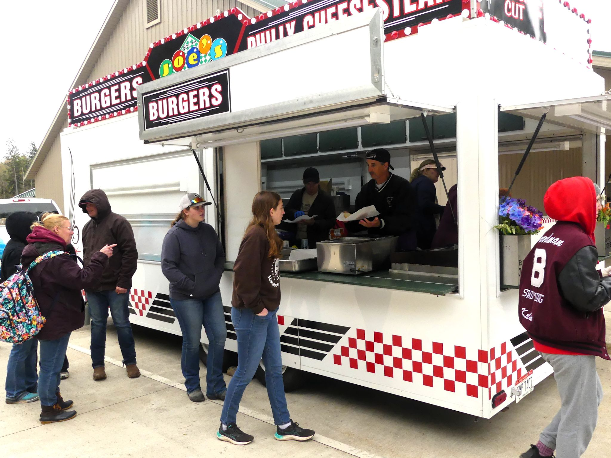 People are ordering food at a burger and cheesesteak stand outdoors.