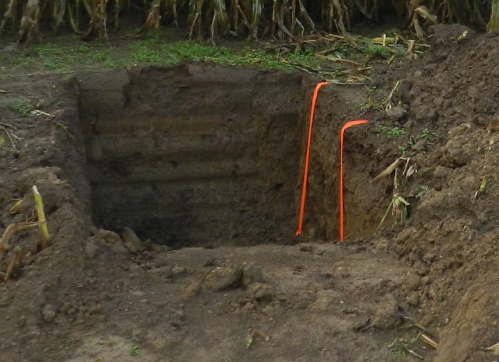 A dug trench or pit with dirt piled around, marked by two orange tapes.