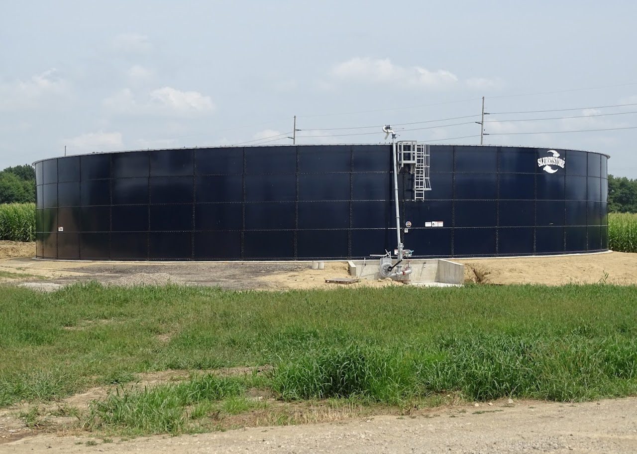 Large circular water storage tank in a grassy area under a cloudy sky.